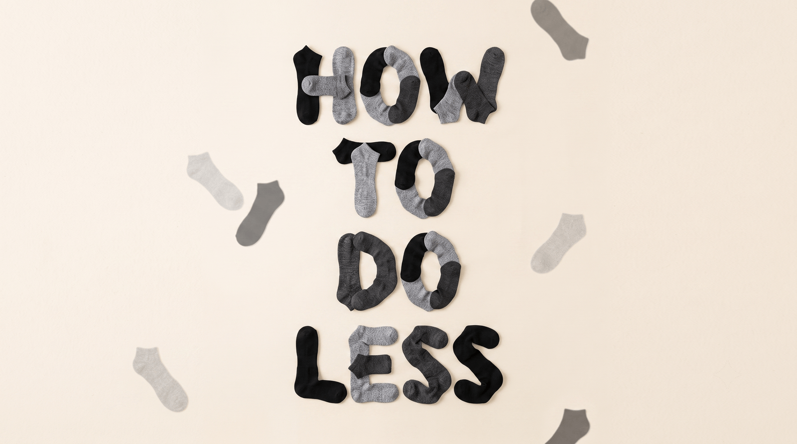 The words "How to Do Less" spelled out from folded ankle socks in dark and light gray on a cream background, surrounded by scattered black, gray, and blue-gray socks.